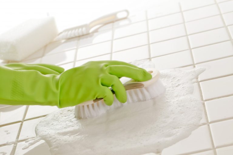 scrubbing tiles with soap while wearing green gloves