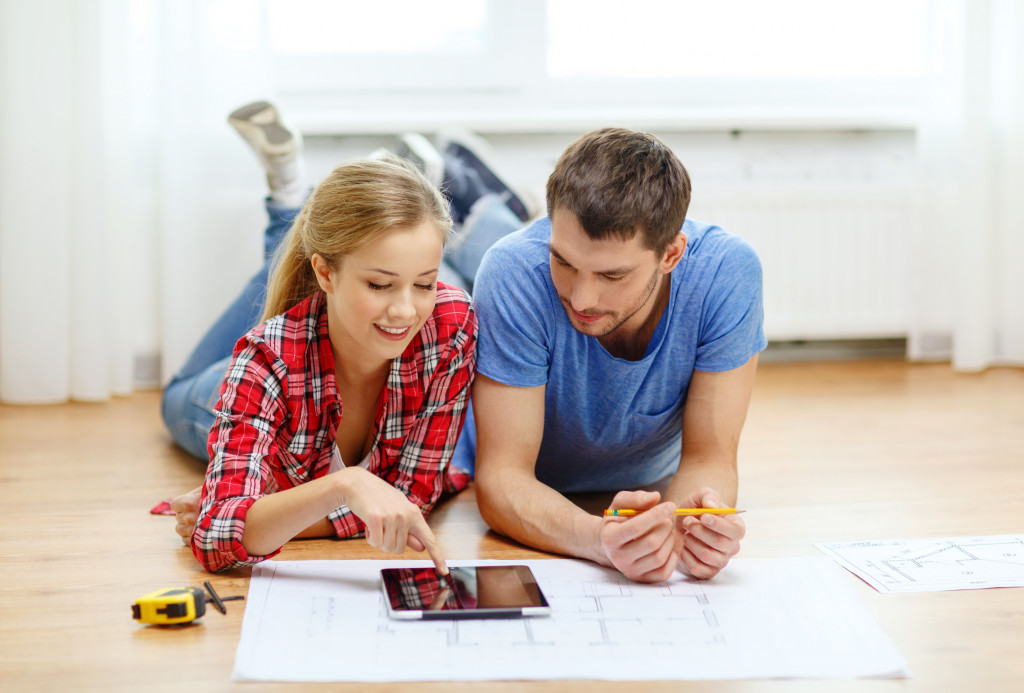 Young couple planning the renovation of their home using a tablet and floor plans.