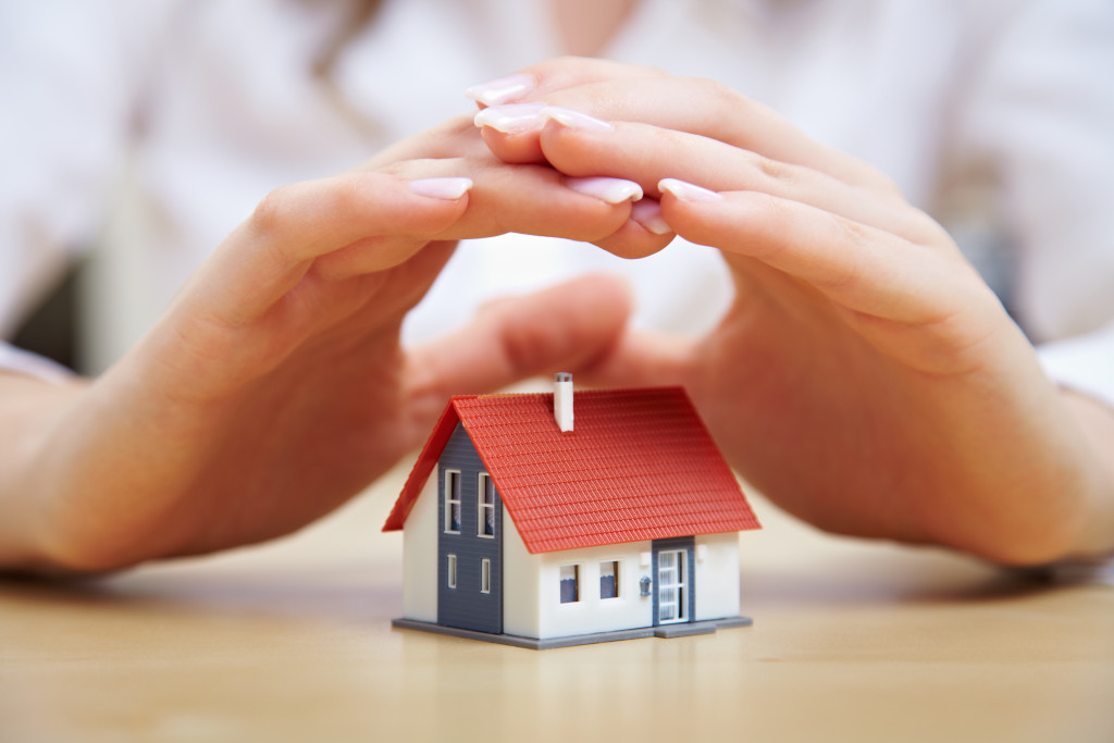 person protecting a miniature house model with her hands representing insurance