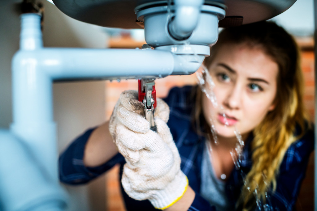 a woman fixing a leaking faucet pipe