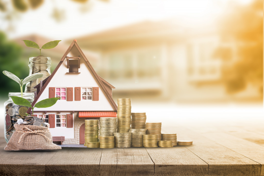 miniature house model with pile of coins on the side and bag of coins with plants